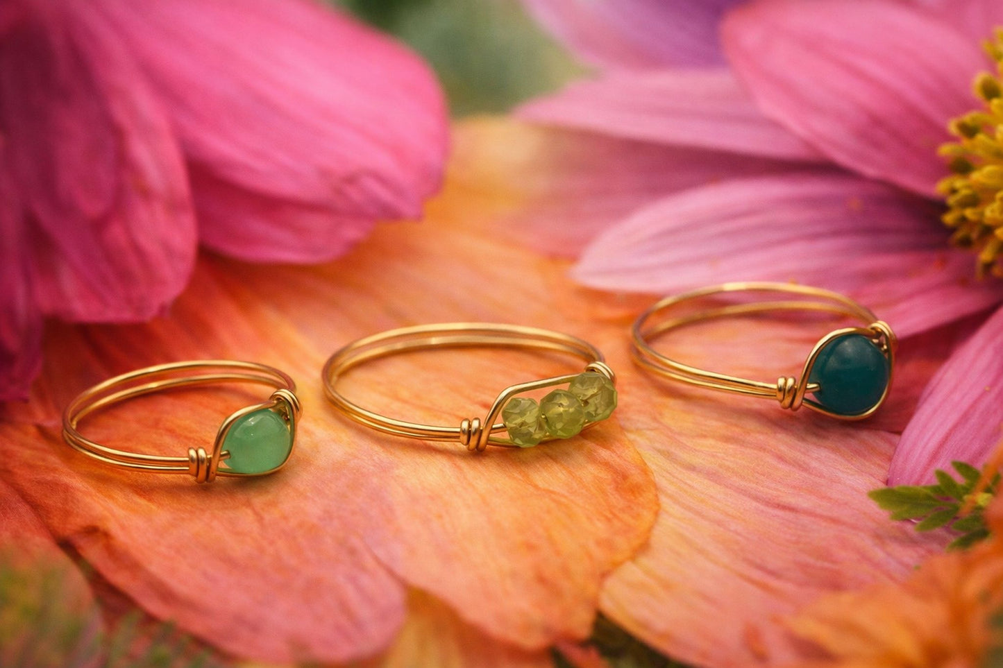 Three gold rings with green gemstones on a pink flower background