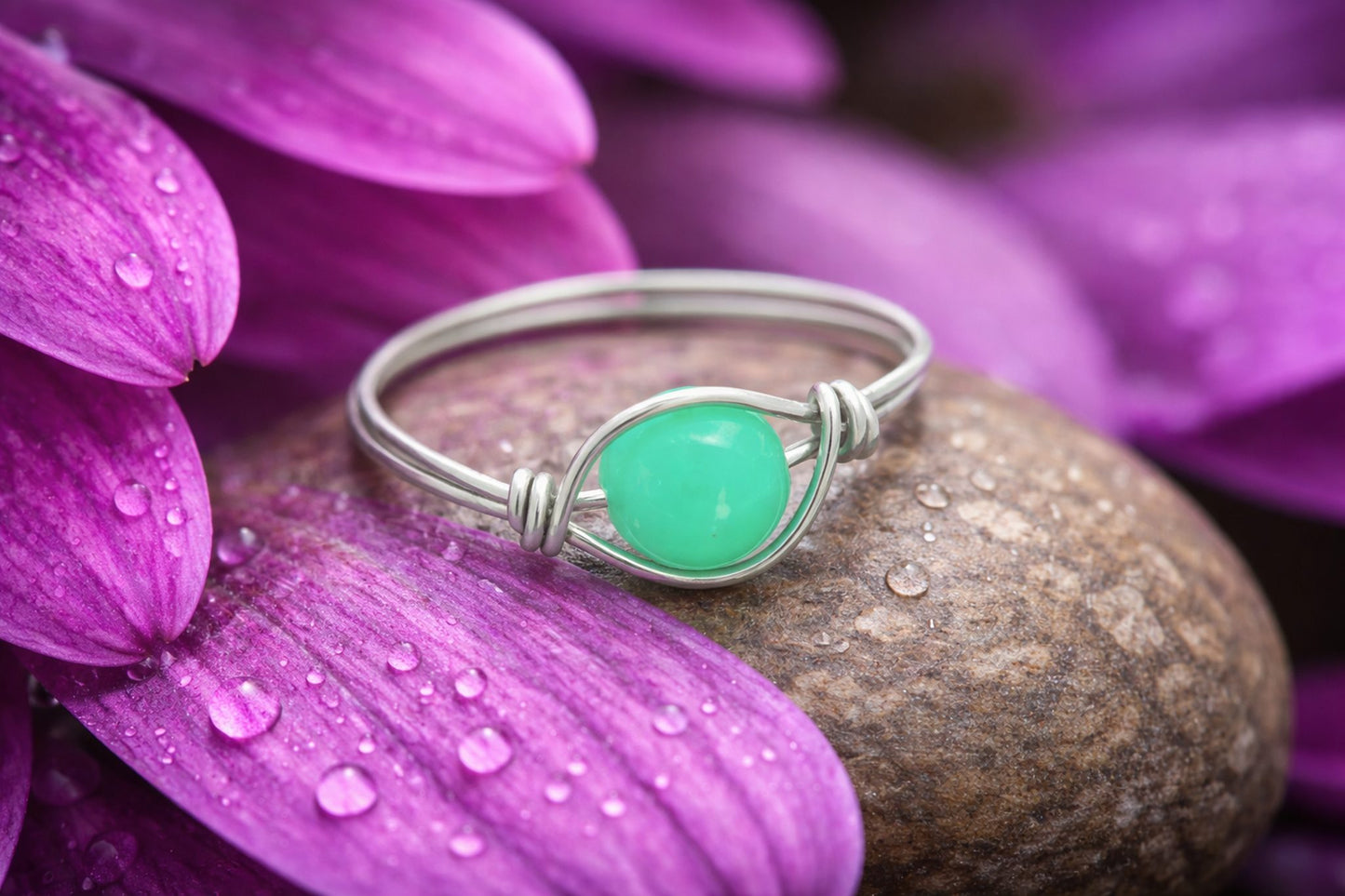 Silver ring with a green gemstone on a purple flower petal